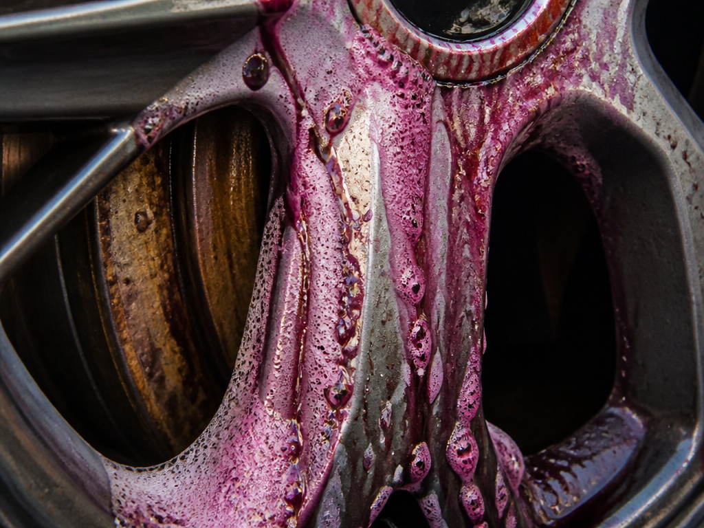 Purple iron remover spray reacting with baked-on brake dust on a car wheel.